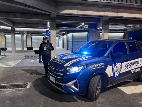 Guardia de ASCOR Security junto al vehículo con la baliza encendida en un estacionamiento techado